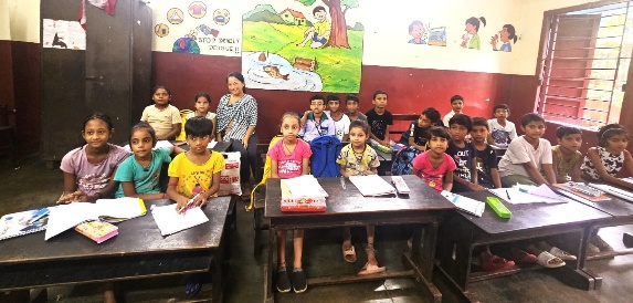 Children seated at wooden desks in an MKSS classroom with educational posters on the wall